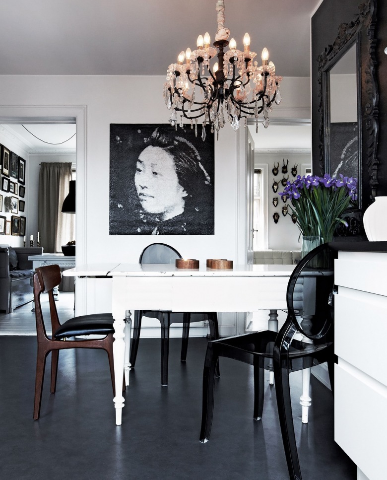 Stylowy żyrandol,biały rozkładany stół w tradycji skandynawskiej,czarne przeźroczyste krzesła z tworzywa,czarna podłoga z  żywicy i czarno-biała fotografia na ścianie (26533)