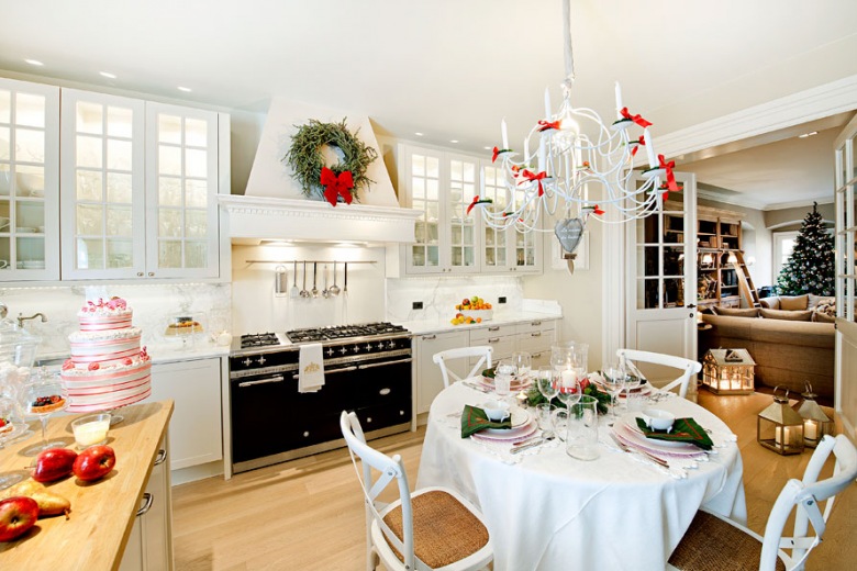 Aranżacja kuchni z jadalnią w białym kolorze. Świąteczne pojedyncze dodatki wnoszą do wnętrza przytulną wigilijną aurę, podobnie jak odświętna zastawa na stole. Podświetlane witrynki w zabudowie kuchennej prezentują się elegancko i pozwalają wyeksponować bardziej ozdobne akcesoria i...