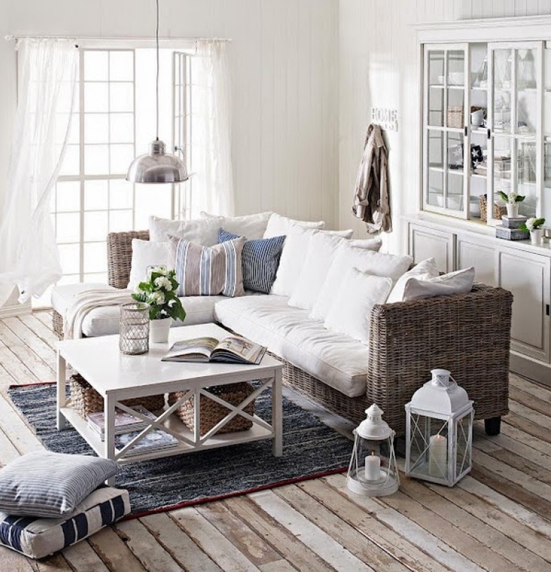 Prosta sofa kanapa z wikliny z białymi i szaro-niebieskimi poduszkami,białe lampiony i latarenki,biały kwadratowy stolik i biała witryna (25069)