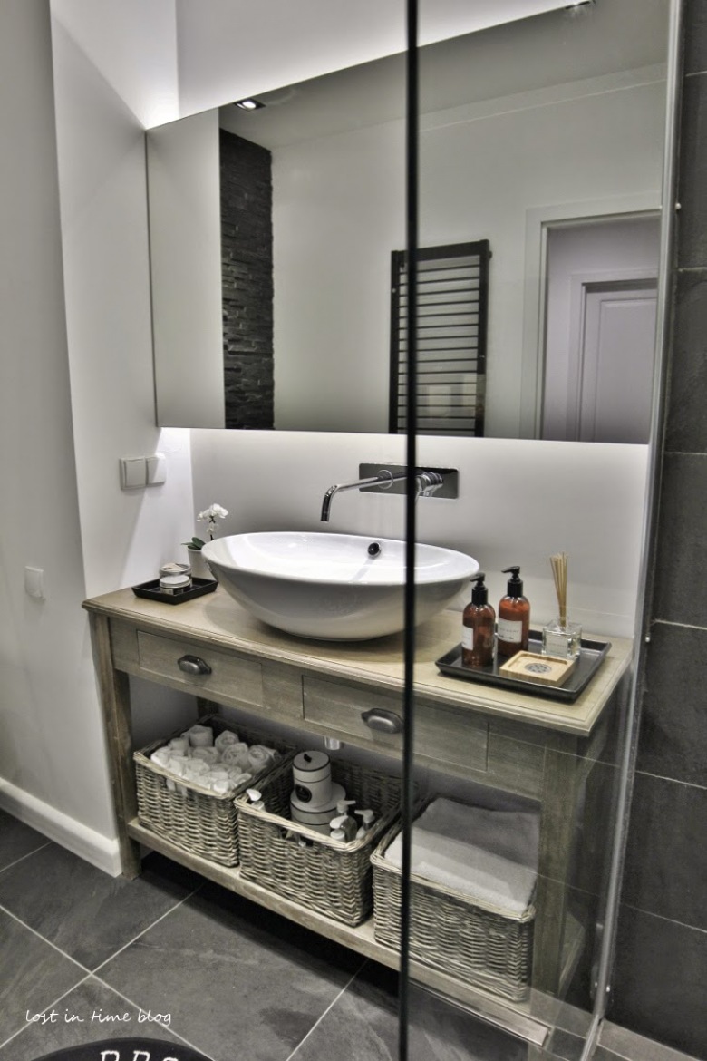 Owalna umywalka na konsolce z półką z bielonego drewna,duża tafla lustra nad umywalką,naścienna nowoczesna bateria,wiklinowe koszyki na ręczniki i akcesoria łazienkowe,szklana kabina z natryskiem (26016)