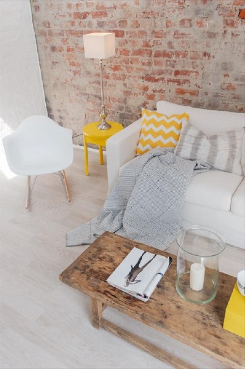 Żółty stolik pomocniczy,poduszki z żółto-białym wzorem szerwonu,drewniany stolik vintage i ściana z cegły (24579)