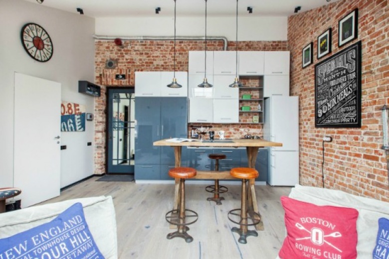 Biało-niebieska kuchnia w otwartym widoku na salon ze ścianą z czerwonej cegły (24069)