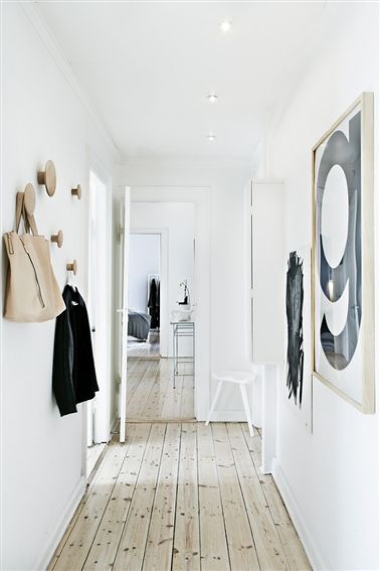 Podłoga olejowana z naturalnego drewna,drewniane wieszaki ścienne grzybki,białe ściany,nowoczesne czarno-białe grafiki na ścianie w wąskim przedpokoju (25797)