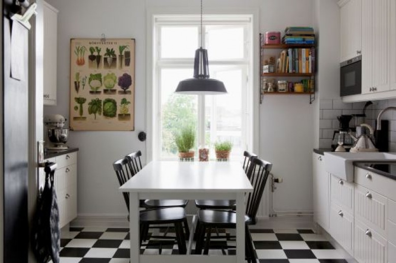 Biało-czarna terakota ułożona w karo w białej kuchni z białym stołem, czarnymi krzeslami i plakatem z ziołami (24527)