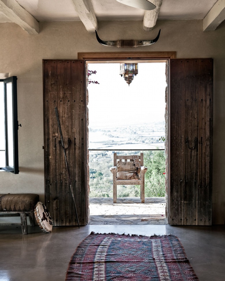 Ciemnobrązowe drewniane drzwi wrota z okuciami z żelaza, betonowe ściany i etniczny dywanik (25385)