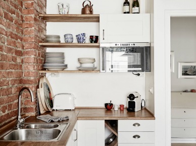 Biała kuchnia skandynawska z drewnianymi blatami i półkami i ścianą z czerwonej cegły (27035)
