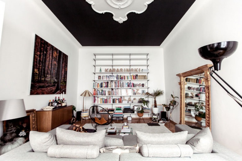 Czarny sufit z białymi ornamentem ze sztukaterii,rzeźbione lustro,nowoczesna biala sofa,i  drewniana komoda w eklektycznym salonie (25581)