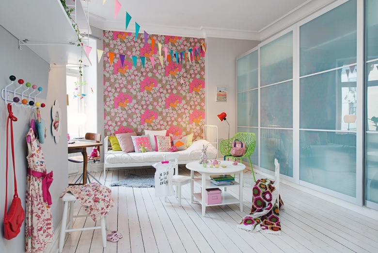 Tapeta ścienna w różowe kwiaty,szafa z przesuwnymi szklanymi i piaskowanymi drzwiami,metalowy wieszak z kolorowymi gałkami i białe mebelki w pokoju dziecięcym (25841)