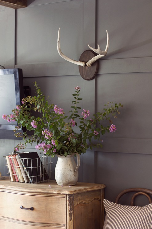 Stylowo udekorowana ściana ze stylową komodą w rustykalnym stylu. Do tego koszyki i piękny wazon z kwiatami.
