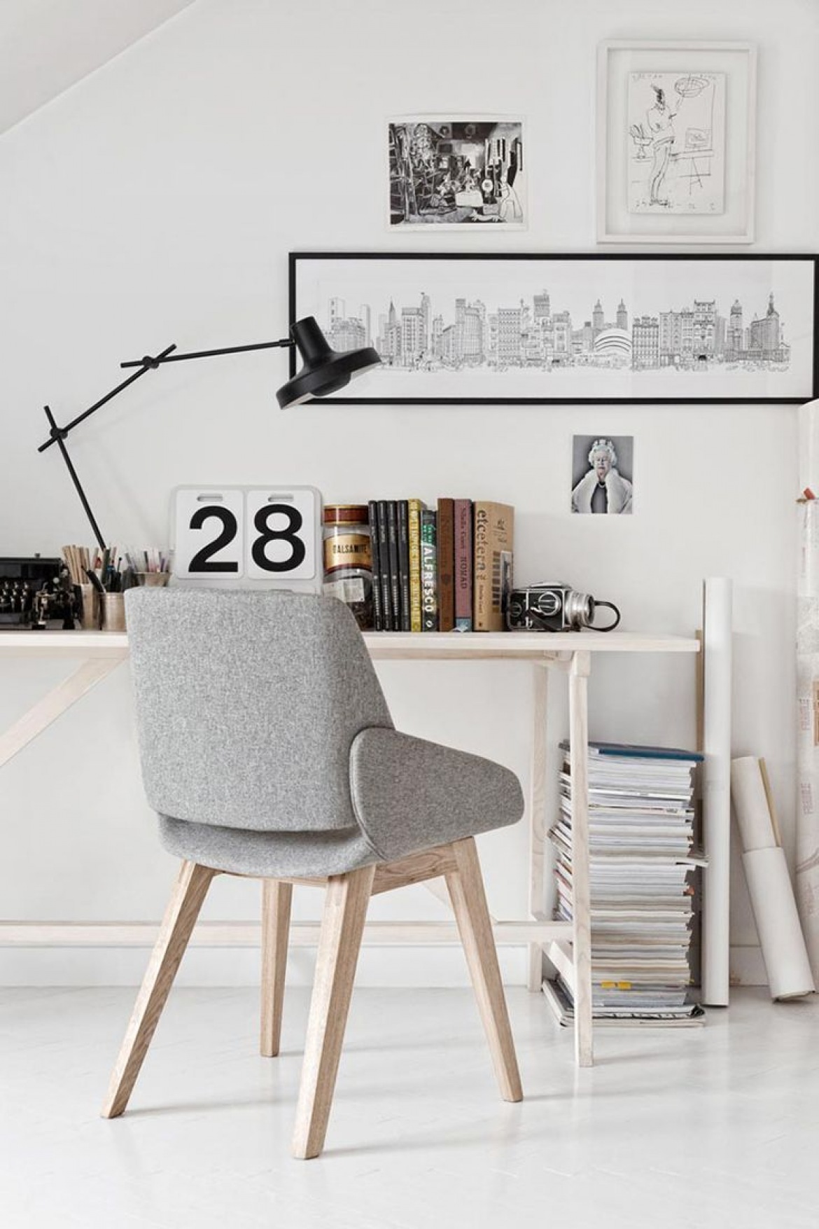 Biały kącik biurowy z nowoczesną czarną lampą, prostym biurkiem,szarym tapicerowanym fotelikiem i biało-czarnymi skandynawskimi grafikami (26126)