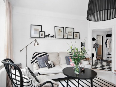 Jasnoszara sofa,czarny bambusowy gięty fotel,biało-czarne poduszki i dywan w paski,okrągły czarny stolik kawowy i czarna lampa wisząca w salonie (26704)