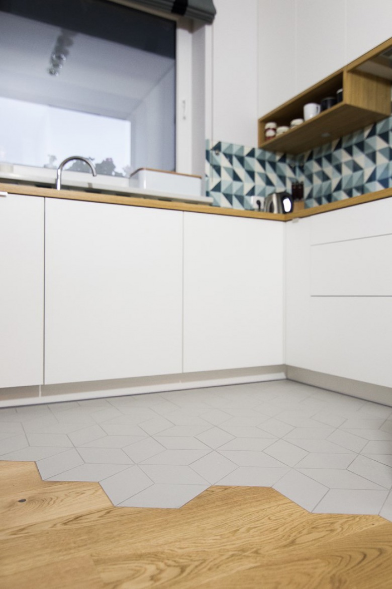 Białe szafki o gładkich frontach bez uchwytów wprowadzają nieco nowoczesnego charakteru do skandynawskiej kuchni. Kompozycja bieli i drewna rozjaśnia przestrzeń i wnosi do niej nieco przytulności. Intensywny geometryczny wzór na ścianie nad blatem w zdecydowany sposób dekoruje...