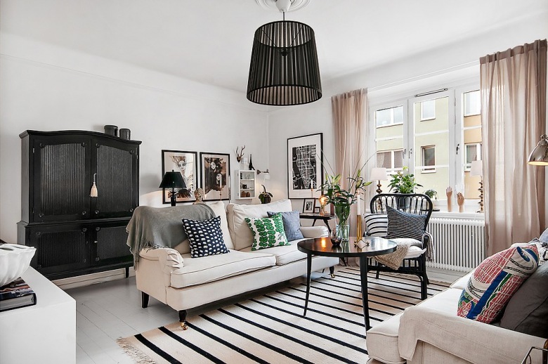 Czarna stylowa komoda z nadstawką,biały dywan w czarne paski,czarny stolik kawowy,graficzne wzory dekoracyjnych poduszek na jasnoszarej sofie w salonie (26702)