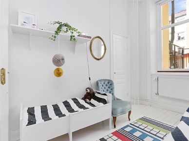 Biało-czarna pościel w paski,białe łóżko z drewna,kolorowy geometryczny dywanik i okrągłe lustro na ścianie w sypialni (26758)
