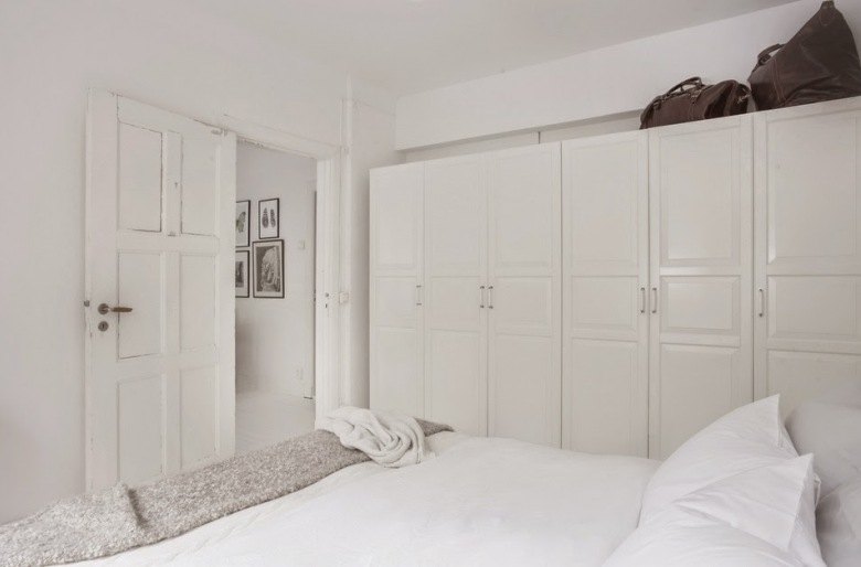 W sypialni ustawiono pojemne białe szafy wzdłuż jednej ściany. Śnieżna paleta barw wprowadza nieco chłodny nastrój, a...