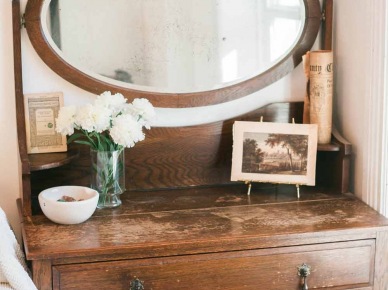 Drewniana komoda bardzo harmonijnie wpisuje się w aranżację sypialni w stylu vintage. Postarzane drewno dodaje wnętrzu charakteru i tworzy spójną całość z wystawionymi na blacie dekoracjami, w tym ze starą rodzinną fotografią czy wiekową...