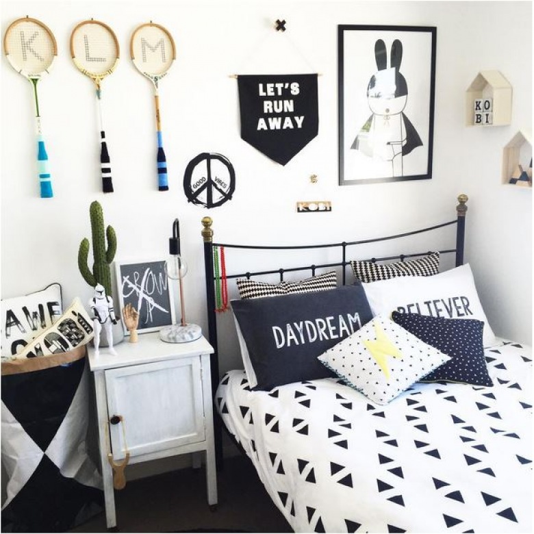 Czarne metalowe łóżko z czarno – białą narzutą i dekoracyjnymi poduszkami w różne wzorki, utrzymane w tej samej...