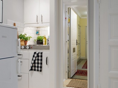 Białe szafki kuchenne ze stalowym blatem w mini aneksie kuchennym w otwartym widoku z przedpokojem z prostokatnym bialym lustrem (25916)