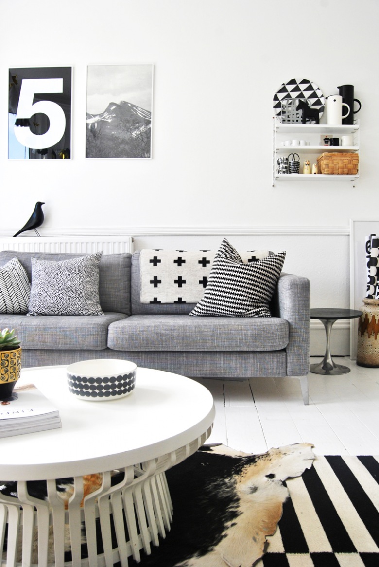 Skandynawski salon z szarą sofą,białą podłogą i grafikami na ścianie (24890)