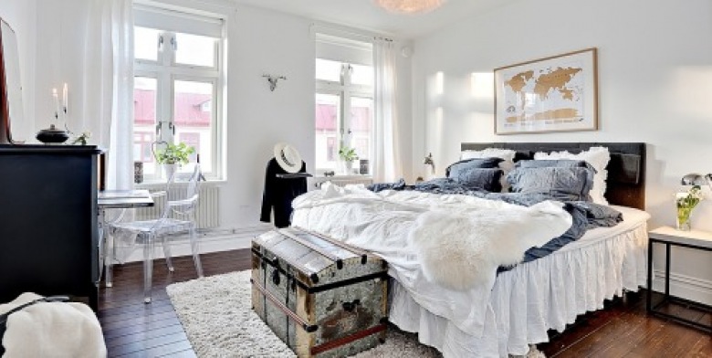Falbany na pościeli, kufer i mapa na ścianie tuz nad łóżkiem buduje bardzo podróżniczy styl tej sypialni.