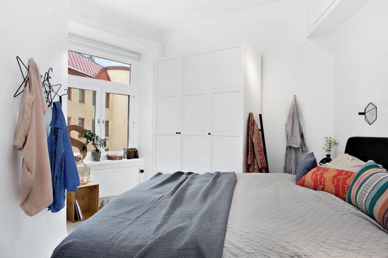 Białe szafy w sypialni z czarnym łóżkiem ubranym w szarą narzutę i kolorowe poduszki ozdobne (25926)