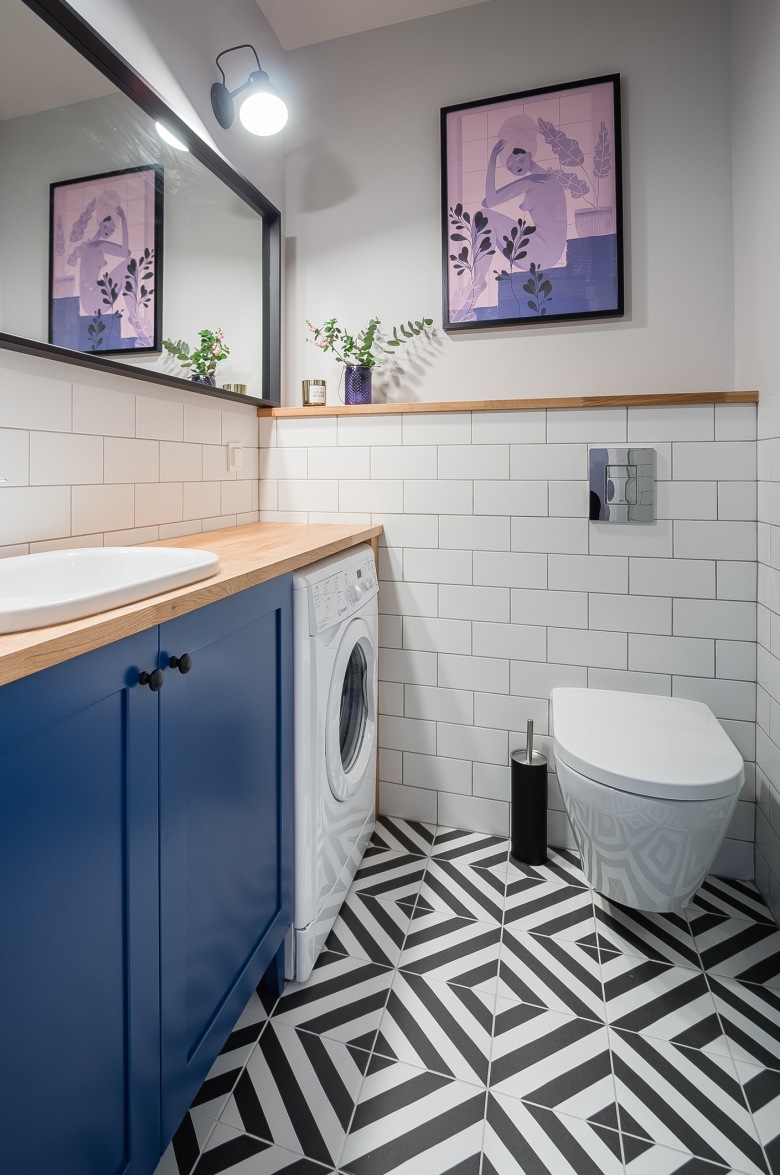 Aranżacja łazienki wygląda inspirująco. Białe ściany, niebieska szafka oraz drobne drewniane detale ładnie uzupełniają...