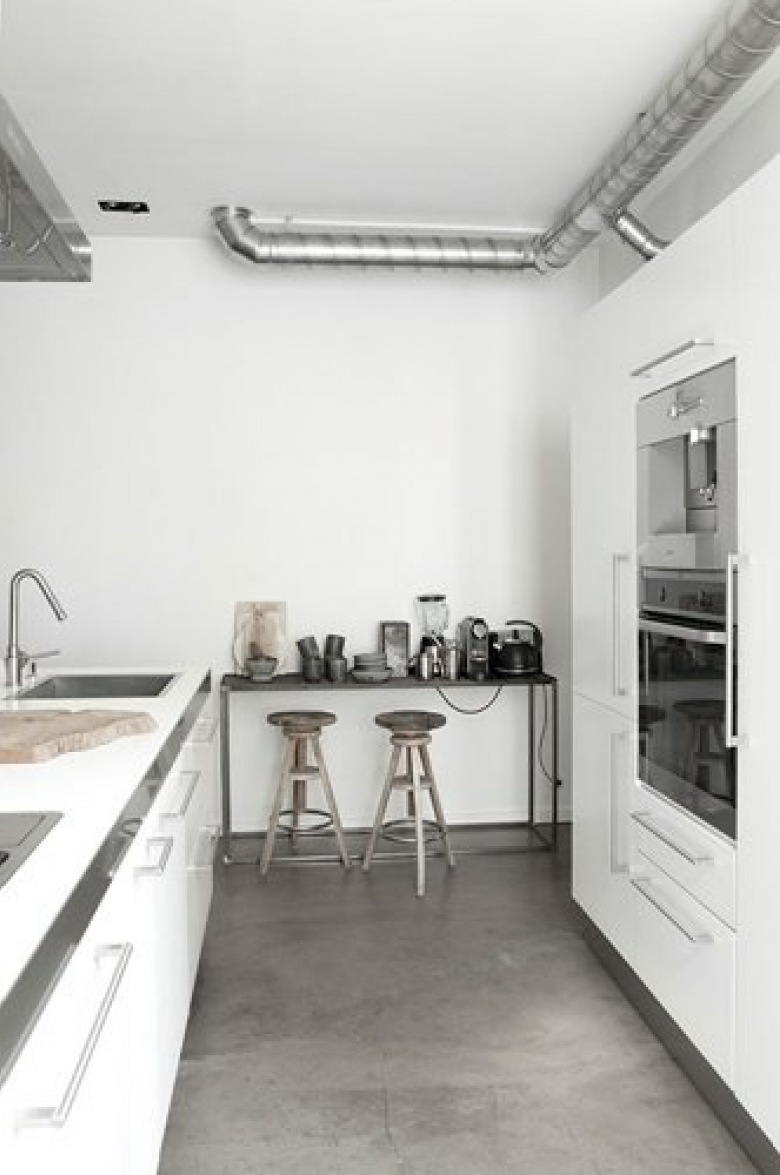 Betonowa posadzka, drewniane stołki i industrialna konsolka w białej kuchni (21149)