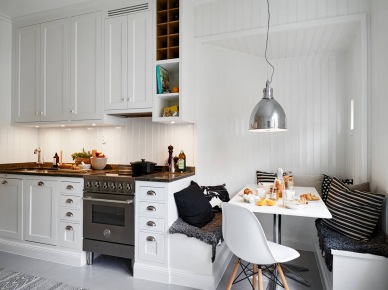 Tradycyjna biała kuchnia skandynawska z zabudowanymi siedziskami, biało-czarnymi poduszkami i srebrną lampą nad stołem (26978)