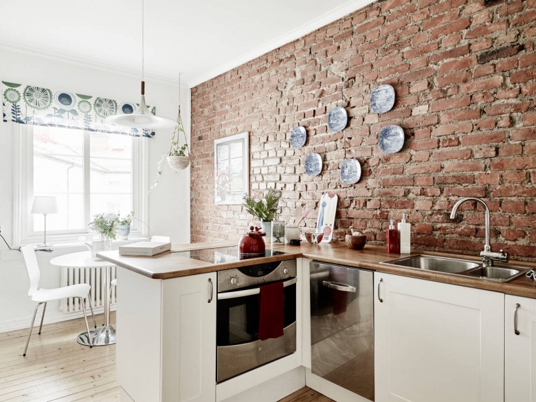 Skandynawska kuchnia z białymi szafkami z drewnianymi blatami i ścianą z czerwonej cegły (27032)