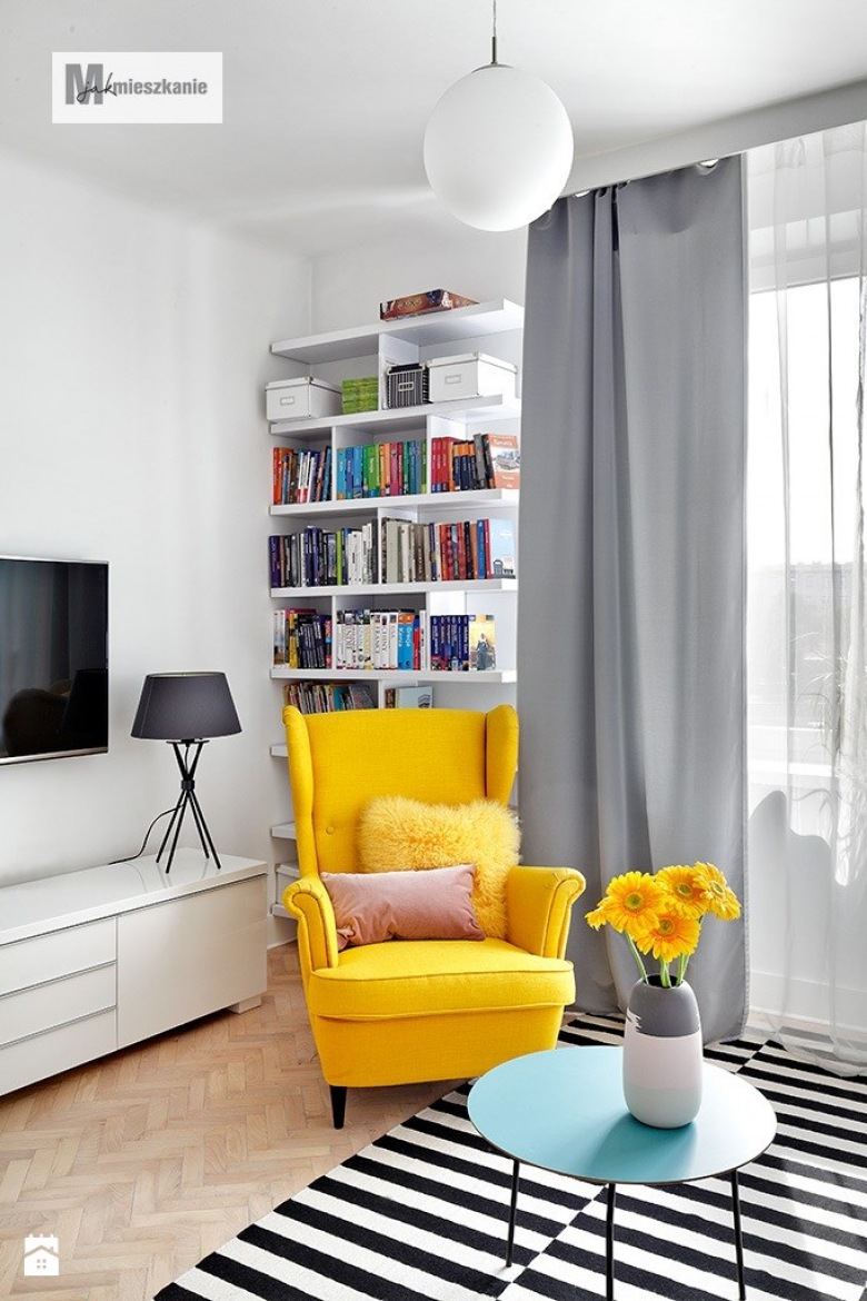 Żółty fotel wraz kolorowymi poduszkami oraz kwiatami w wazonie dominują w tym nowoczesnym, utrzymanym w stosnowanych...