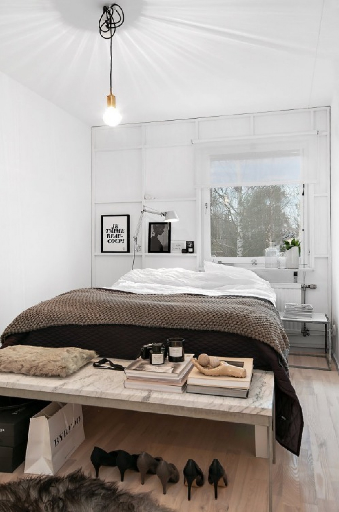 Żarówka na kablu,industrialne białe panele na ścianie,kamienna ławka ze szklanymi bokami i czarno-białe grafiki w skandynawskiej sypialni (27387)