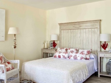 Drewniane bielone łóżko,biały wiklinowy fotel i parkiet w stylu vintage w sypialni z lampkami z czerwonego koralowca (25014)