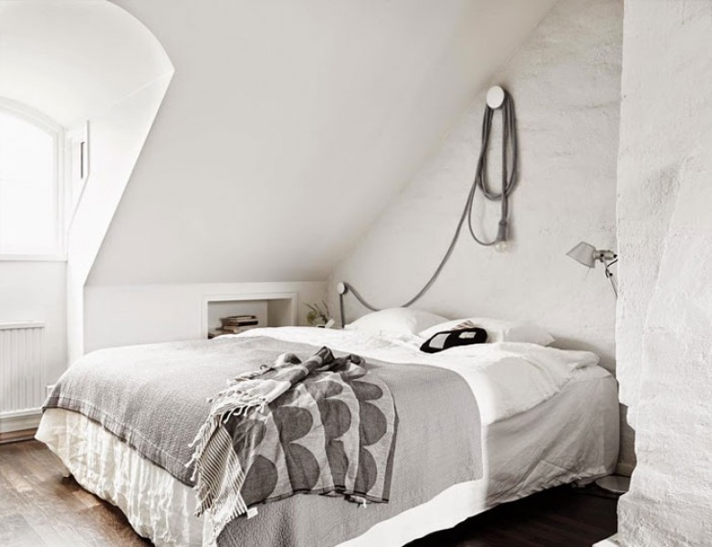 Biało-szara narzuta na łóżku w skandynawskiej sypialni z ciekawym mocowaniem żarówki na kablu na ścianie nad łóżkiem (26620)
