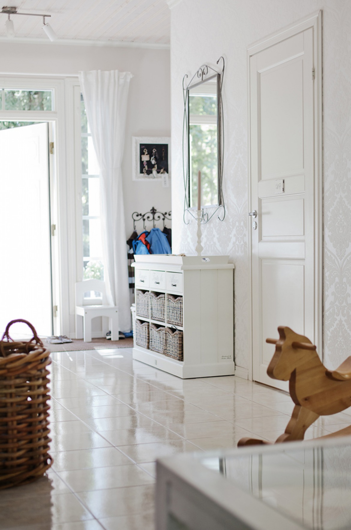 Biała komoda z drewna i wiklinowymi koszykami pod kutym lustrem na ścianie (21934)