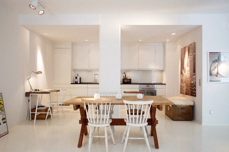 piękny i minimalistyczny przykład połączenia kilku pomieszczeń na jednej przestrzeni - to skandynawski salon razem z kuchnią i jadalnią. Mamy nieskazitelną biel, surowe palety z drewna, proste formy drewnianych mebli i nieodparty urok...