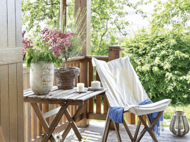 Drewniany stolik na krzyżaku i drewniany fotel skandynawski z białym płótnem,lampiony i rustykalne osłonki na kwiaty na wiejskiej werandzie (24840)