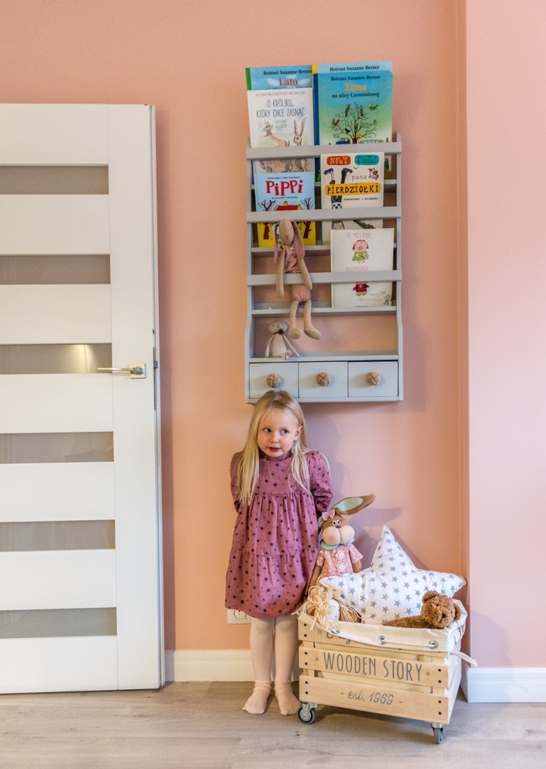 W pokoju dziecięcym jedna ze ścian pomalowano na różowy pudrowy kolor. Na niej zawieszono wąską półeczkę z praktycznymi...