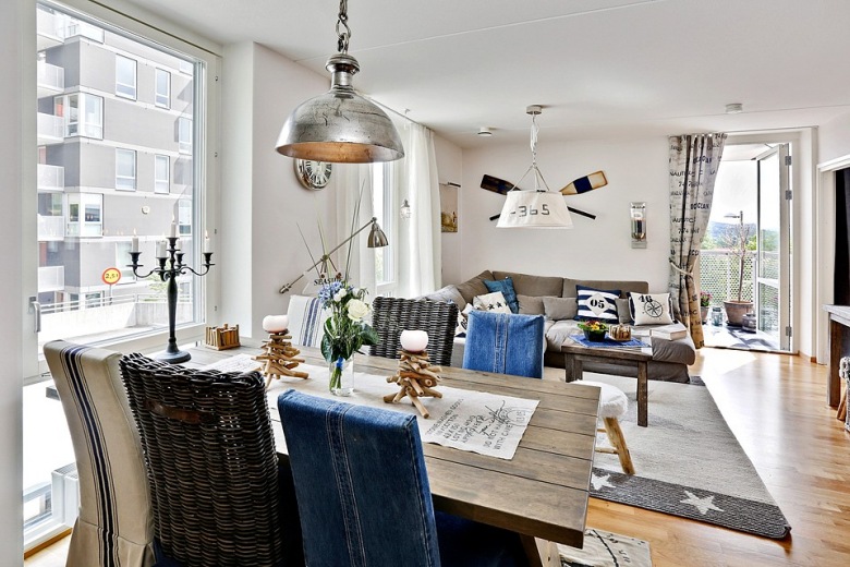 bardzo oryginalne mieszkanie i ciekawe - choć to kolejny przykład mieszkania w stylu skandynawskim, to wyróżnia je pomysł na ubranie krzeseł w dżinsowe ubranka. Zmiksowane krzesła w wysokimi oparciami pochodzą z różnych stylów i wykonane zostały z różnych materiałów. Mamy więc niebieski dżins, wyplatany rattan i industrialną tapicerkę z francuską nutką. Krzesła stoją w otwartym widoku salonu przy drewnianym stole na kozłach i stanowią centralny punkt mieszkania i dekoracji tej otwartej przestrzeni. Oprócz kolorów błękitnego dżinsu panuje biel i subtelne szarości - w szlachetnej tapicerce narożnika, przetartym drewnie stolika kawowego i metalowej lampie z industrialną nutką. Ten niejednorodny styl nadał temu wnętrzu oryginalności  i niebanalności....
