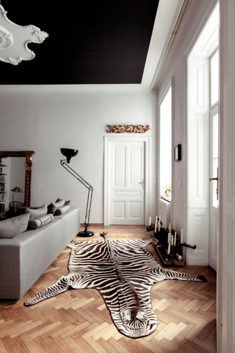 Czarno-biały dywan zebra, nowoczesna biala sofa,industrialna czarna lampa podłogowa i rzexbione stylowe lustro w aranżacji salonu z czarnym sufitem (25578)