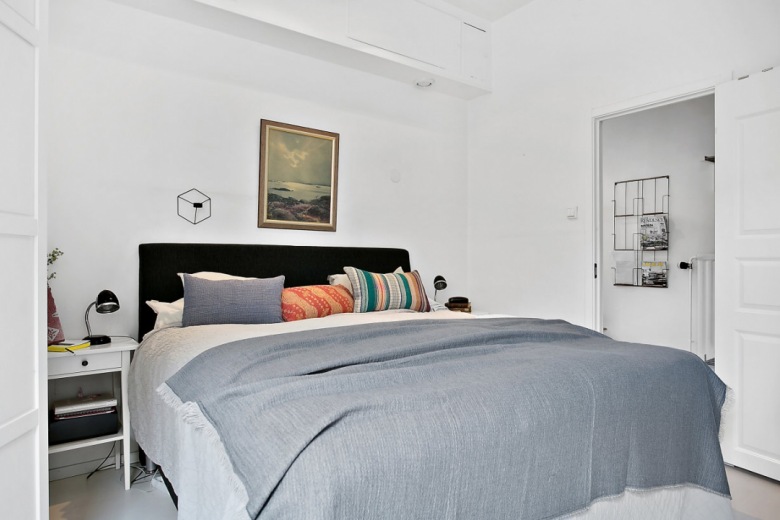 Szara narzuta,czarne tapicerowane łóżko,białe stoliki nocne i obraz retro na białej ścianie w sypialni (25920)