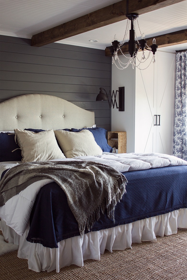 Żyrandol w sypialni i drewniane belki to bardzo odważny duet. Do tego eleganckie łóżko z bezowym zagłówkiem i poduchami...