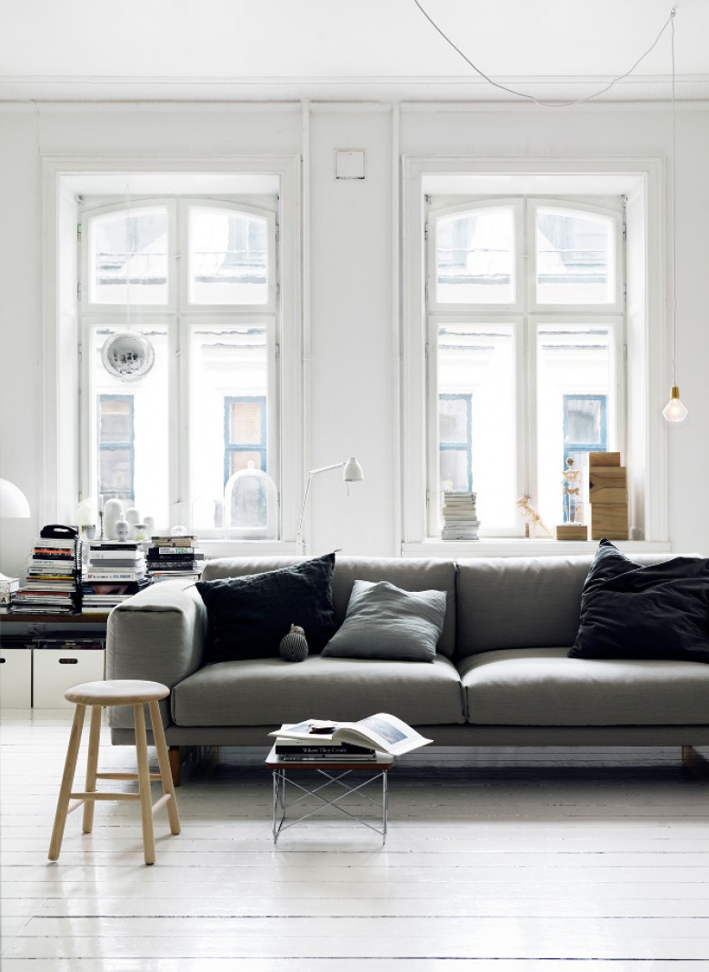 Biały salon z szarą sofą ubraną w czarne poduszki (20774)