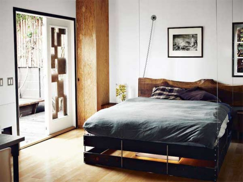 genialny pomysł na urządzenie jednopokojowego mieszkania - w tej prostej, męskiej aranżacji łóżko wylądowało przy suficie. Z chwilą potrzeby opuszczane jest na podłogę na linach i zasłonięte zasłoną - rewelacyjny pomysł do małych mieszkań o ograniczonej powierzchni użytkowej. Poza tym ta mała przestrzeń jest ciekawie zaaranżowana z wyjątkowym umiłowaniem prostoty, drewna i czarnego koloru....
