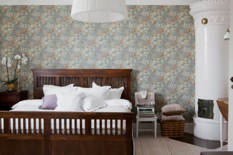 Kolonialne drewniane łóżko,ceramiczny skandynawski piec i tapeta z wmotywem kwiatowym w aranżacji sypialni (24531)