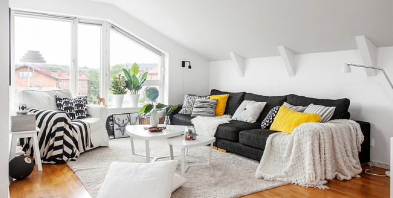 Grafitowa sofa z żółtymi i biało-czarnymi poduszkami,biały stolik,biały futrzak dywan i pld w czarno-białe pasy w dekoracji salonu (25734)