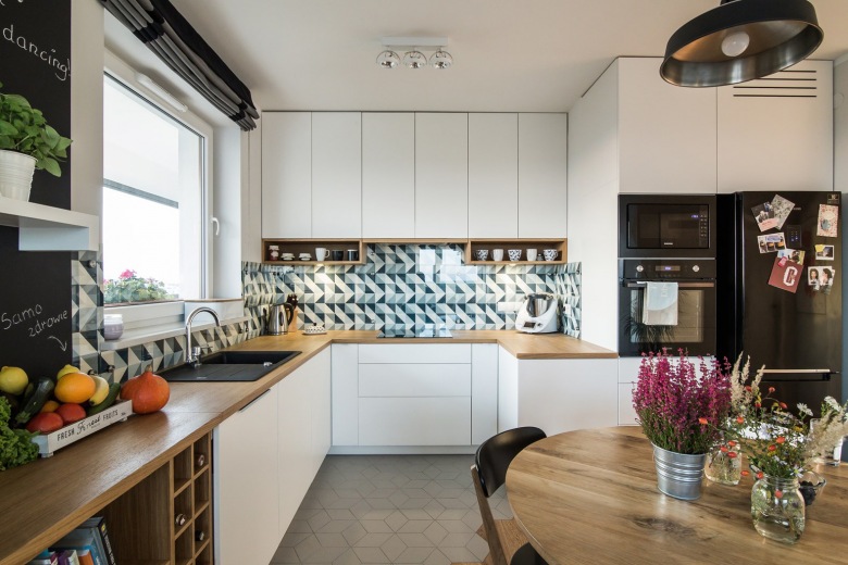 Prosta zabudowa kuchenna łączy funkcjonalność stylu skandynawskiego z nowoczesną formą, potęgowaną dodatkowo przez geometryczne motywy na ścianie. Elementy drewna, takie jak stół czy blat w przyjemny sposób wprowadzają do wnętrza naturalny...
