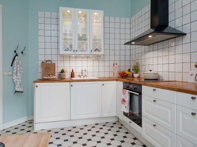 Biała kwadratowa glazura na turkusowej ścianie w białej kuchni skandynawskiej z czarnym okapem i bialo-czarną terakotą na podłodze (25871)