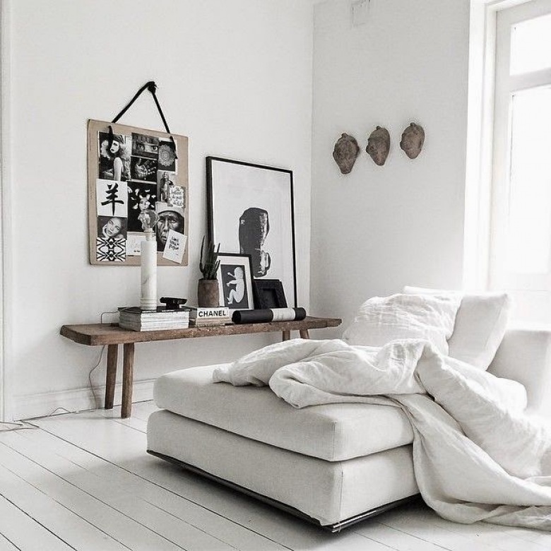 Biała podloga z desek,białe ściany i biała sofa w aranżacji skandynawskiego salonu z drewnianą ławką i czarno-białymi fotografiami i grafikami (25687)