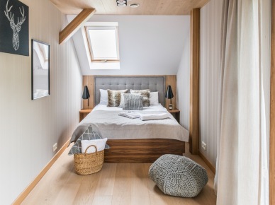 Okno dachowe zapewnia dostęp naturalnego światła, chociaż kolorystyka wnętrza i tak jest dość jasna. Drewniane łóżko z pikowanym wezgłowiem stanowi główny element aranżacji sypialni na...