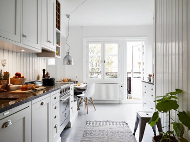 Tradycyjna biała kuchnia skandynawska z zabudowanymi siedziskami, biało-czarnymi poduszkami, srebrną lampą nad stołem i białą boazerią na ścianach (26977)